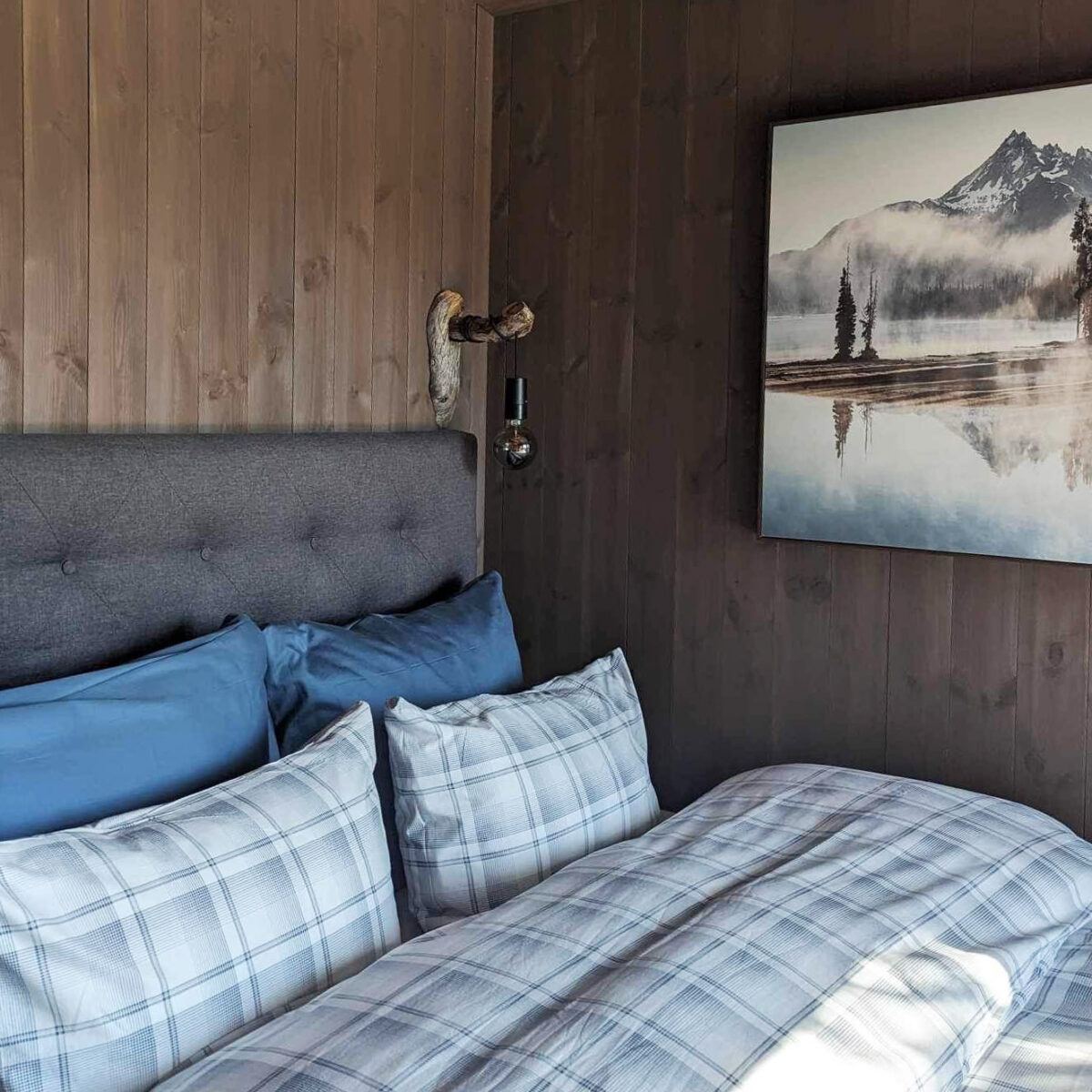 En dobbeltseng med med fint oppredt sengetøy. brune trevegger står tett intill sengen.