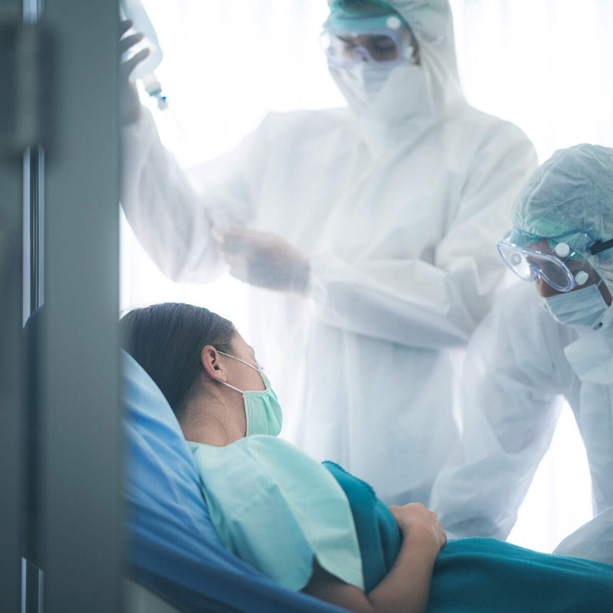 A patient in a hospital lying in a bed and two nurses wearing protective equipment